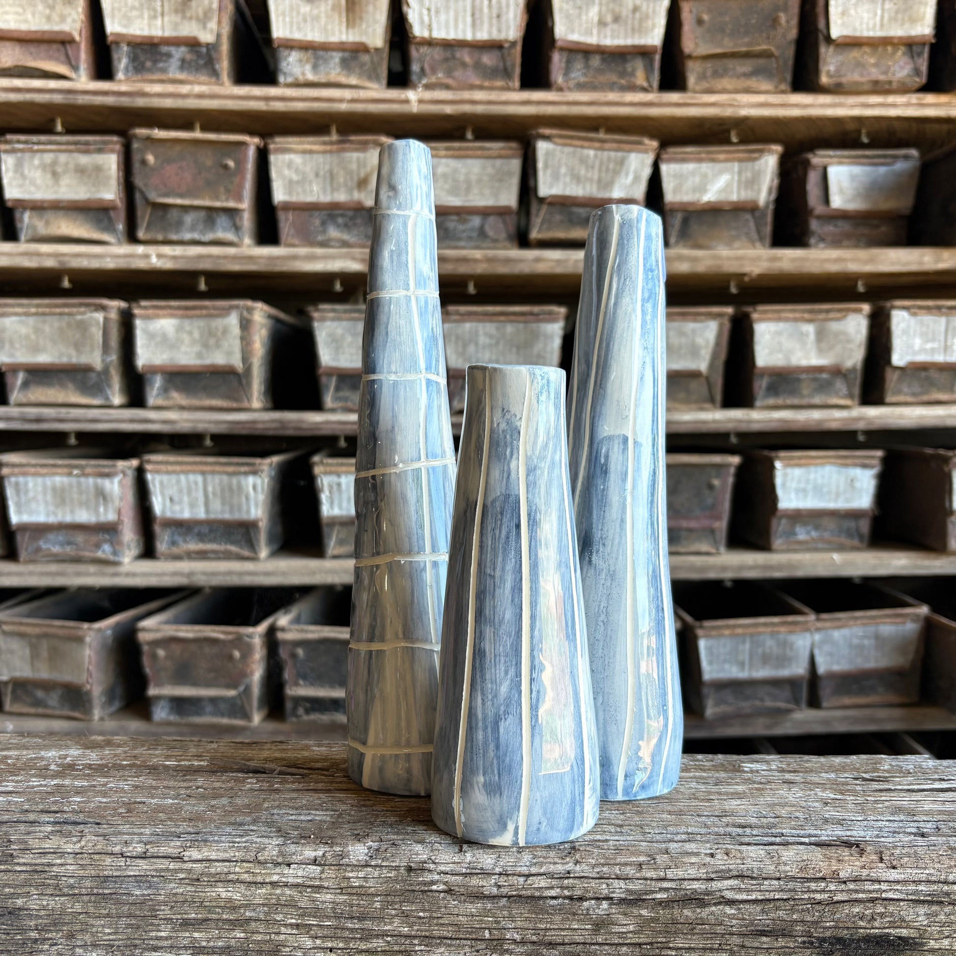 Three wooden vases with striped pattern on a wooden surface with metal trays in the background