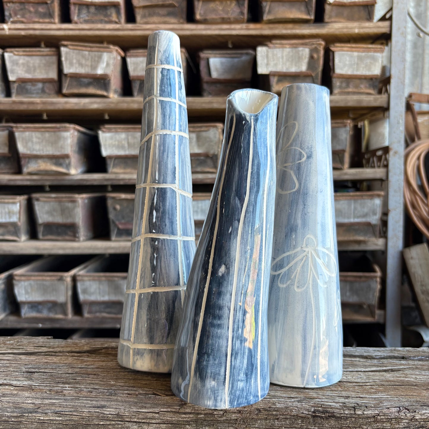 Three wooden vases with engraved designs on a wooden surface with metal trays in the background.